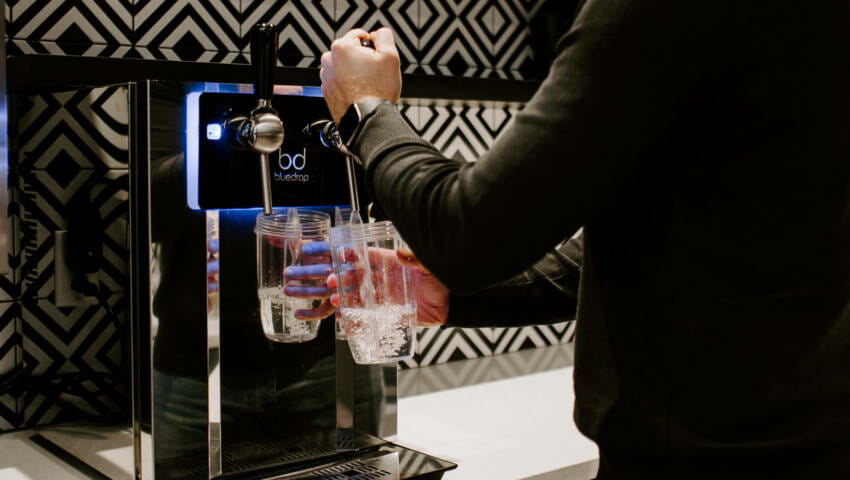 A person using the bluedrop water system to fill a glass of water.