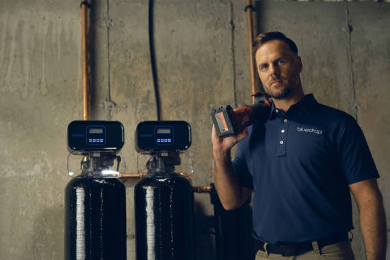 man holding a drill next to bluedrop filter system.